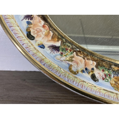 27 - A vintage R. Capodimonte porcelain framed oval wall mirror with cherub design, signed to reverse R.S... 