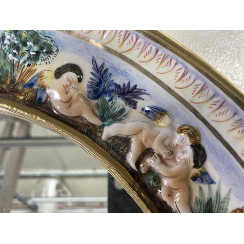 27 - A vintage R. Capodimonte porcelain framed oval wall mirror with cherub design, signed to reverse R.S... 