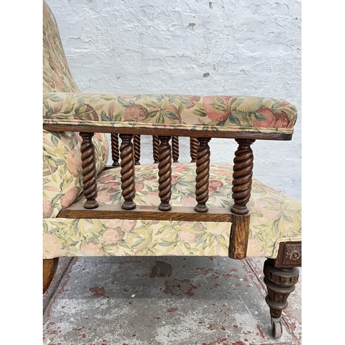 1010 - An early 20th century oak and floral upholstered armchair with barley twist design and brass castors... 