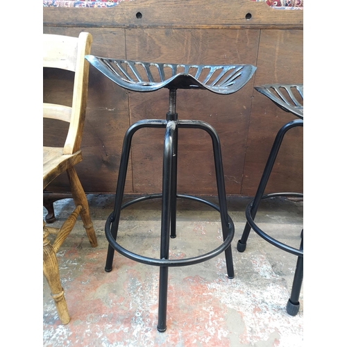 1050 - A pair of black metal tractor seat revolving bar stools - approx. 69cm high