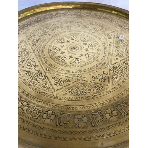 444 - Three items, two brass circular trays - approx. 58cm in diameter and one wooden folding travel table