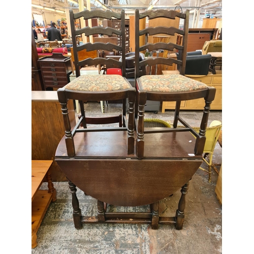 113 - An oak drop leaf gate leg dining table and two ladder back dining chairs