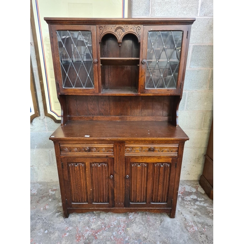 144 - An oak linenfold dresser with two upper leaded glass doors, two drawers and two lower cupboard doors... 