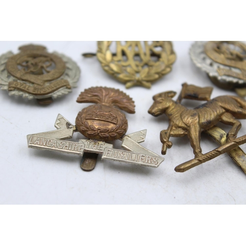 1185 - Ten military cap badges to include The Lancashire Fusiliers, The Devonshire Regiment etc.