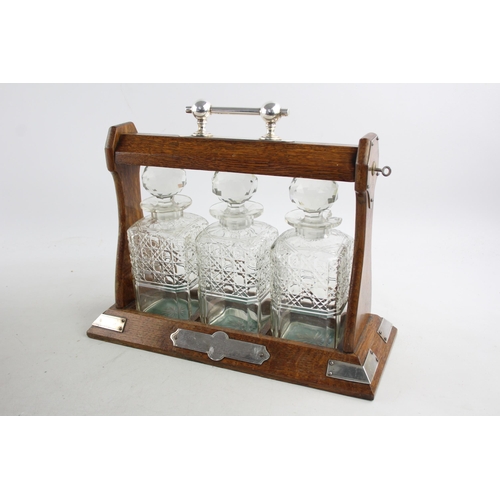 493 - An early 20th century oak and silver plated tantalus with three cut glass decanters