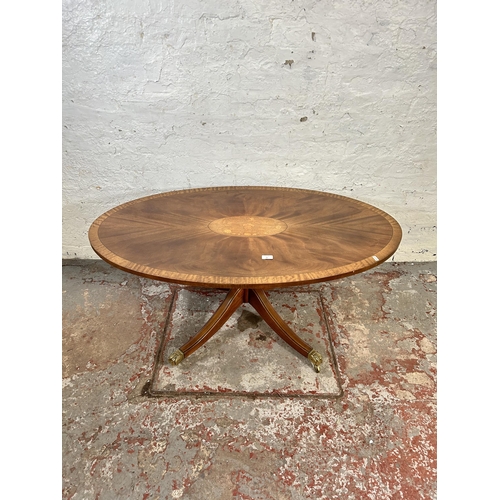 60 - A Regency style inlaid satinwood effect oval coffee table with brass lion paw supports and castors -... 