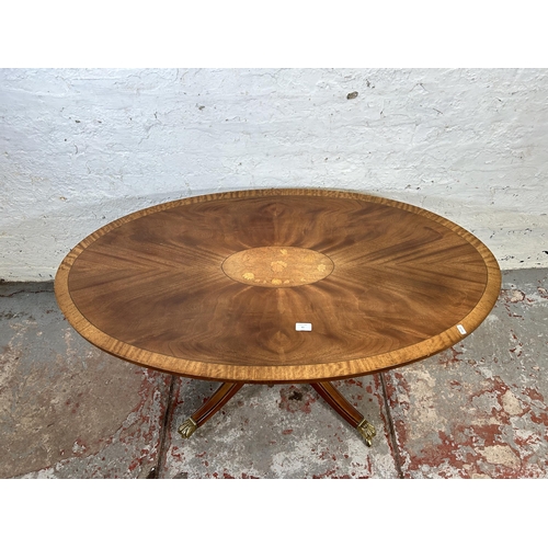 60 - A Regency style inlaid satinwood effect oval coffee table with brass lion paw supports and castors -... 