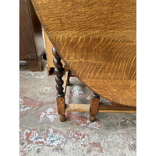 29 - An early/mid 20th century oak drop leaf gate leg oval dining table on barley twist supports