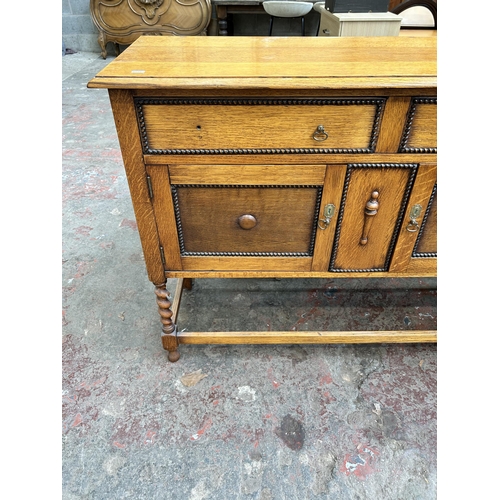 60 - An early 20th century oak sideboard with beaded decoration and barley twist supports