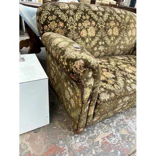 217 - A 1930s floral upholstered drop arm sofa on mahogany supports and castors