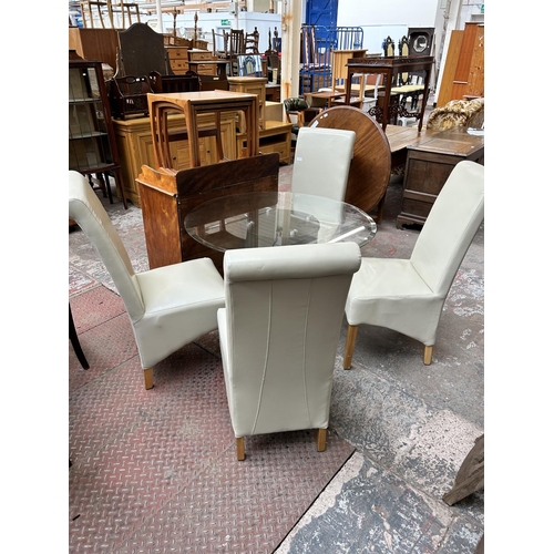 53 - A modern glass top circular dining table on brown leatherette pedestal base and four cream leatheret... 