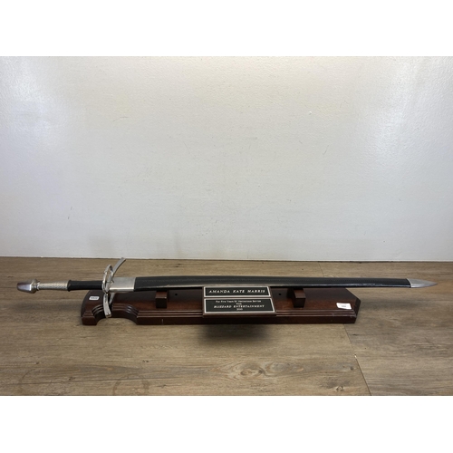 501 - A presentation sword with black leather scabbard on oak stand - presented to Amanda Kate Harris for ... 