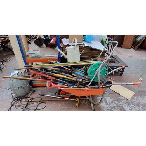 851 - A wheelbarrow containing a large collection of garden tools to include pitchforks, hoes, spades etc.