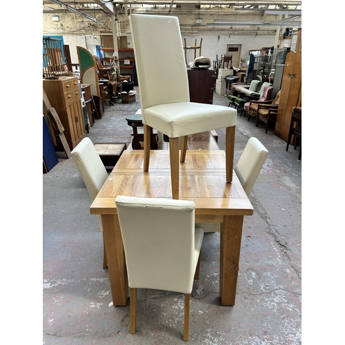 128 - A modern solid oak extending dining table and four cream leatherette dining chairs - table approx. 8... 