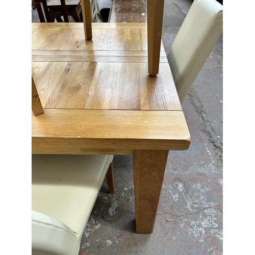 128 - A modern solid oak extending dining table and four cream leatherette dining chairs - table approx. 8... 