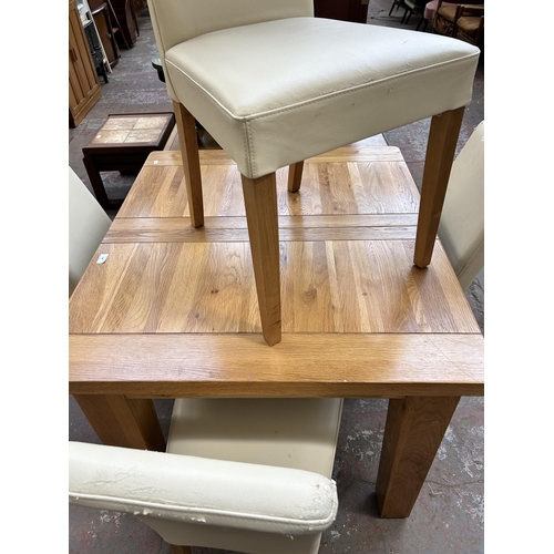 128 - A modern solid oak extending dining table and four cream leatherette dining chairs - table approx. 8... 