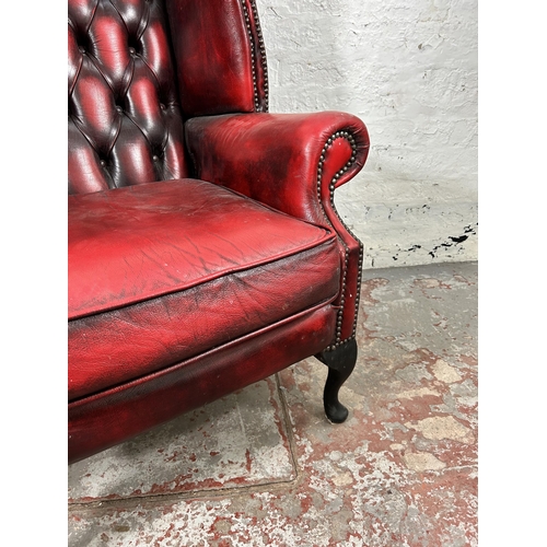 33 - An oxblood leather Chesterfield wingback armchair with cabriole supports