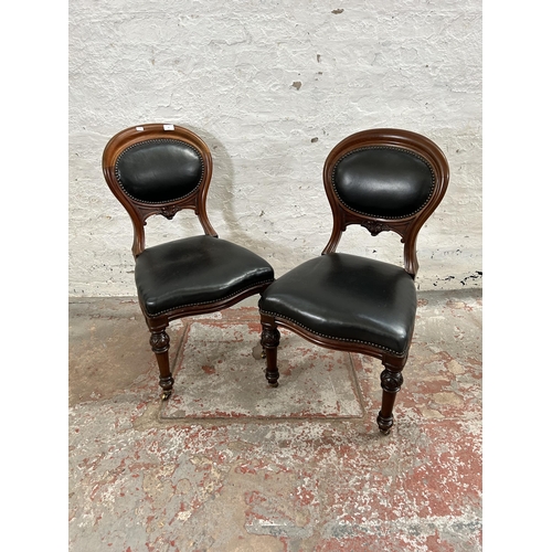 70 - A pair of Victorian carved mahogany and black vinyl balloon back dining chairs with brass castors