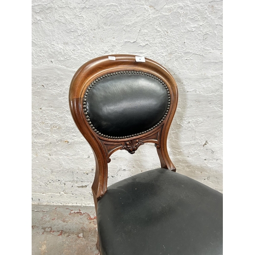 70 - A pair of Victorian carved mahogany and black vinyl balloon back dining chairs with brass castors