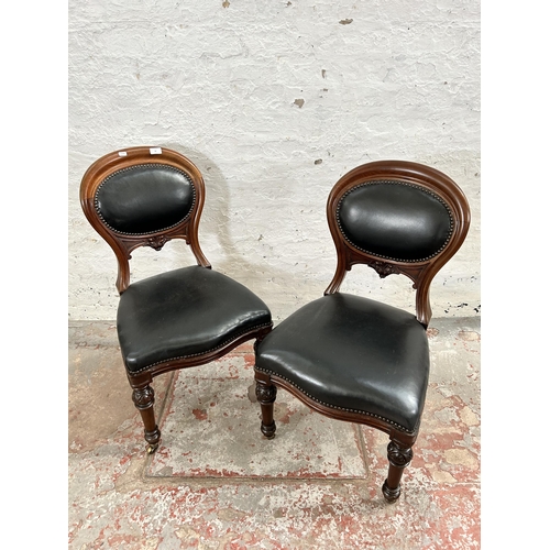 70 - A pair of Victorian carved mahogany and black vinyl balloon back dining chairs with brass castors