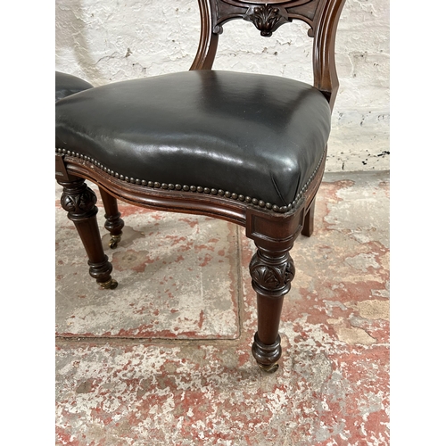 70 - A pair of Victorian carved mahogany and black vinyl balloon back dining chairs with brass castors