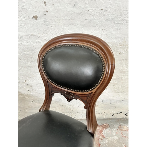 70 - A pair of Victorian carved mahogany and black vinyl balloon back dining chairs with brass castors