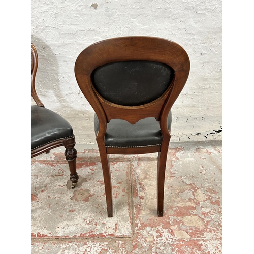 70 - A pair of Victorian carved mahogany and black vinyl balloon back dining chairs with brass castors