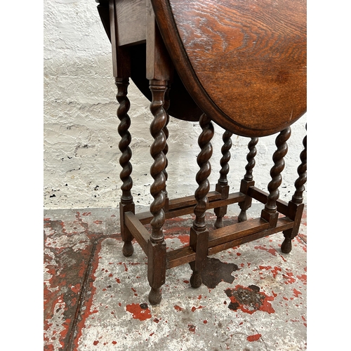 106 - An early/mid 20th century oak drop leaf gate leg oval occasional table on barley twist supports