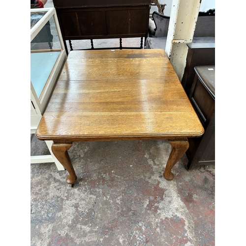 154 - An early 20th century oak rectangular wind out dining table with cabriole supports and winder