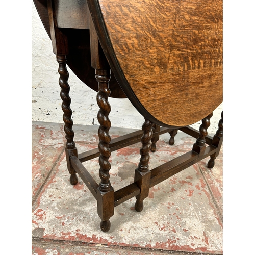 115 - An oak drop leaf gate leg oval occasional table on barley twist supports