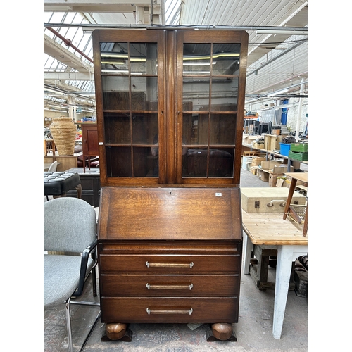 148 - An Art Deco style oak bureau bookcase with two upper glazed doors, fall front, three drawers and bal... 