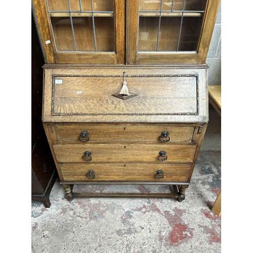 35 - An early 20th century carved oak bureau bookcase with two upper stained and leaded glass doors, fall... 