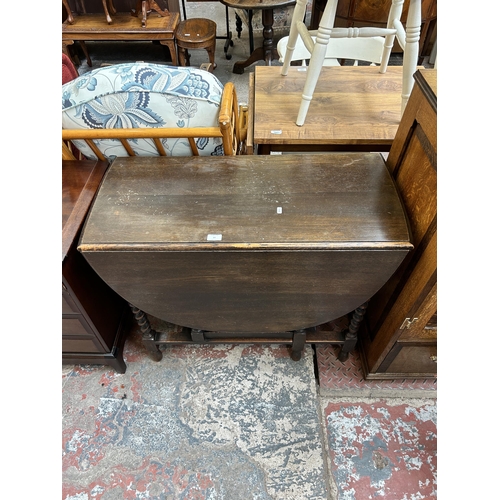 64 - An early 20th century oak drop leaf gate leg oval dining table on barley twist supports