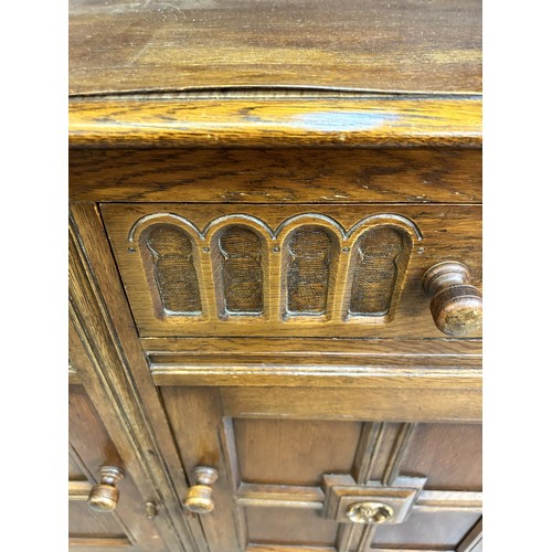 46 - An L. Marcus Ltd carved oak dresser with arched two tier plate rack, two drawers and two cupboard do... 