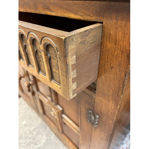 46 - An L. Marcus Ltd carved oak dresser with arched two tier plate rack, two drawers and two cupboard do... 