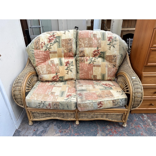 135 - A wicker and cane two seater conservatory sofa with floral upholstery