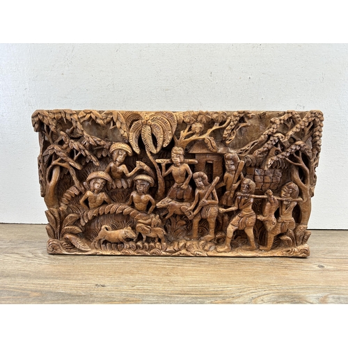 517 - A heavily carved hardwood plaque of a tribal scene - approx. 26cm high x 45cm wide