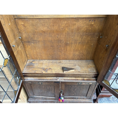 217 - An Arts & Crafts oak bookcase with two leaded and stained glass doors and copper hinges - approx. 19... 