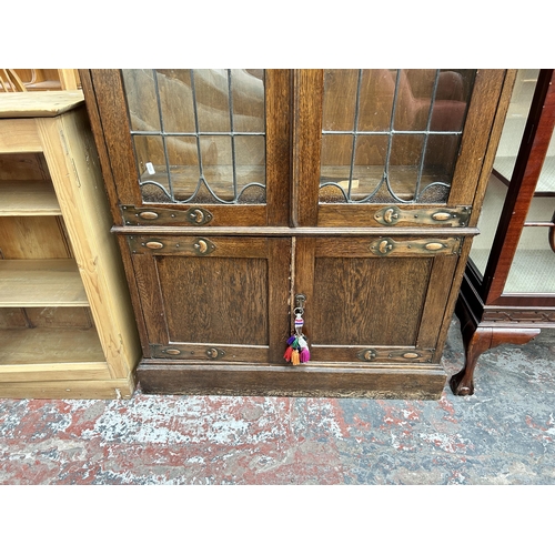 217 - An Arts & Crafts oak bookcase with two leaded and stained glass doors and copper hinges - approx. 19... 