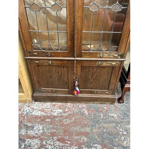 217 - An Arts & Crafts oak bookcase with two leaded and stained glass doors and copper hinges - approx. 19... 