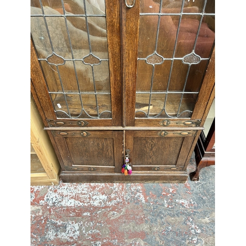 217 - An Arts & Crafts oak bookcase with two leaded and stained glass doors and copper hinges - approx. 19... 