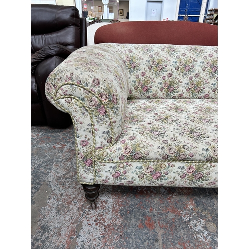 240 - A Victorian floral upholstered three seater sofa with turned wooden supports and castors - approx. 7... 