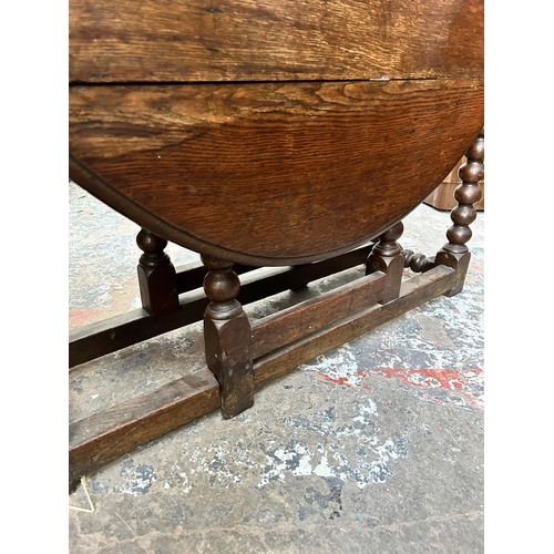 16 - A Georgian oak drop leaf gate leg oval dining table on bobbin turned supports