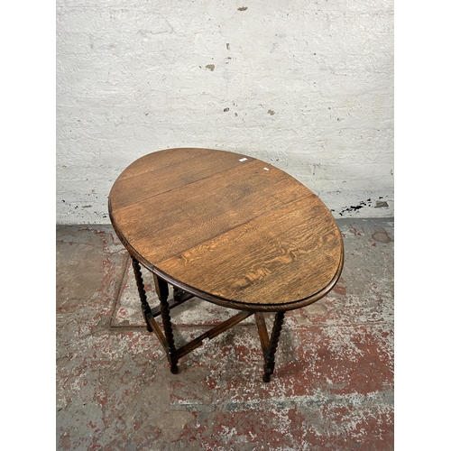 184 - An early 20th century oak drop leaf gate leg oval occasional table on barley twist supports