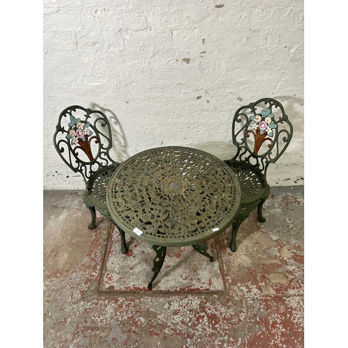 160 - A green painted cast iron patio table and two chairs - approx. 67cm high x 62cm diameter