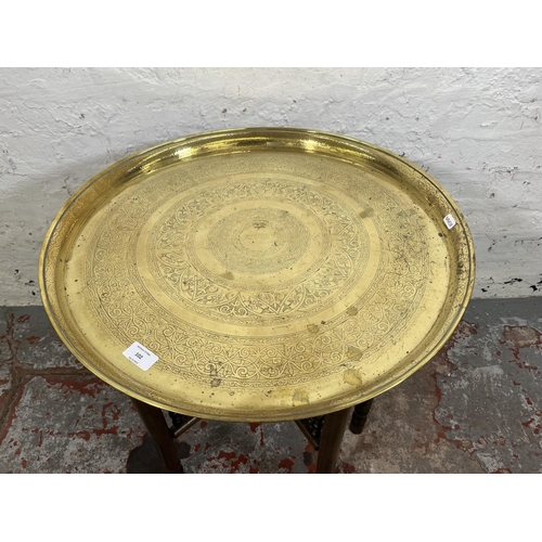 102 - An Indian hardwood collapsible travel table with brass circular tray - approx. 58cm high x 56cm diam... 