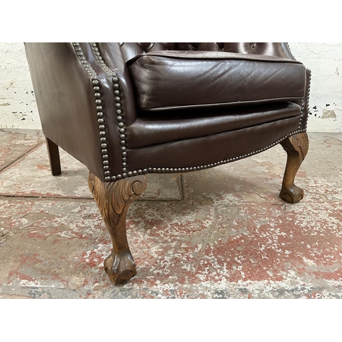 13 - A brown leather Chesterfield wingback armchair on ball and claw supports