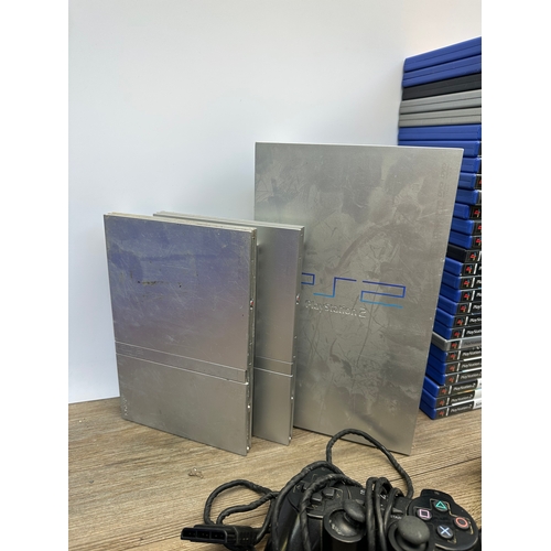 692 - Three silver Sony PlayStation 2 consoles, controllers and games to include The Getaway, The Sims 2 a... 