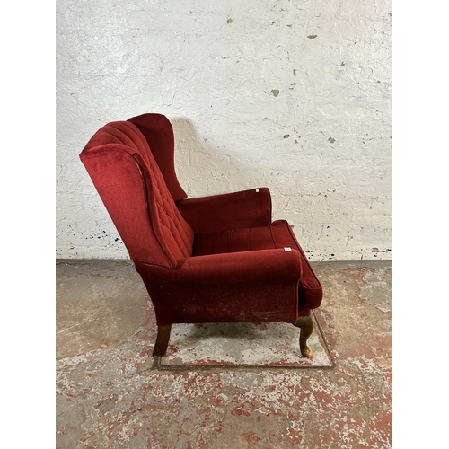 132 - A red fabric upholstered wing back armchair on cabriole supports