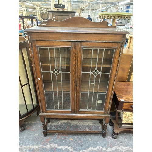 172 - An early 20th century oak display cabinet with two lead and stained glass doors on barley twist supp... 